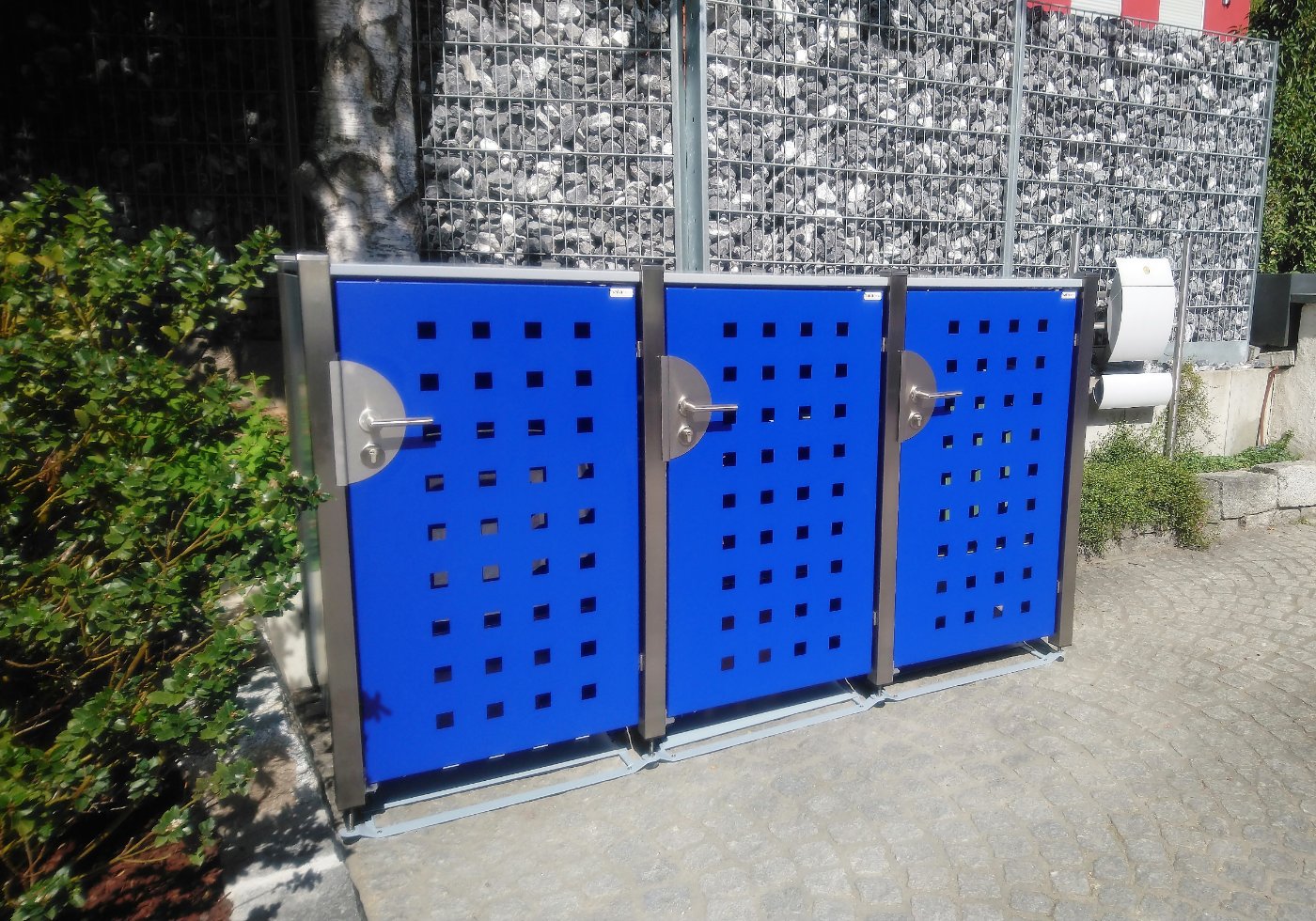 Dreifach-Anlage HALABOX Modular mit blauen Türen und Quadrat-Lasermuster vor einer Gabionenwand
