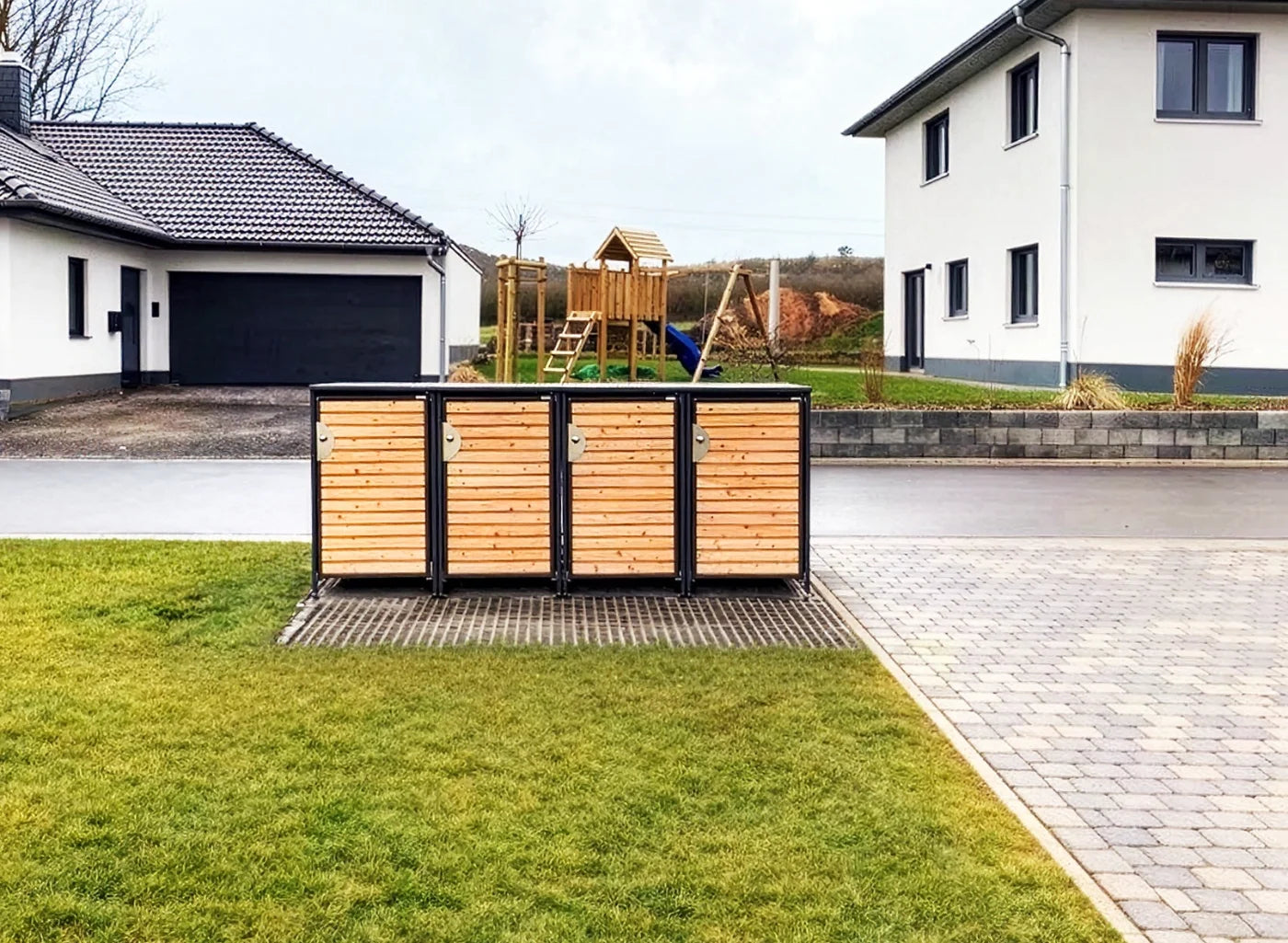 Vierfach-Anlage HALABOX Modular mit Türfüllung aus Lärchenholz vor einem Neubaugrundstück