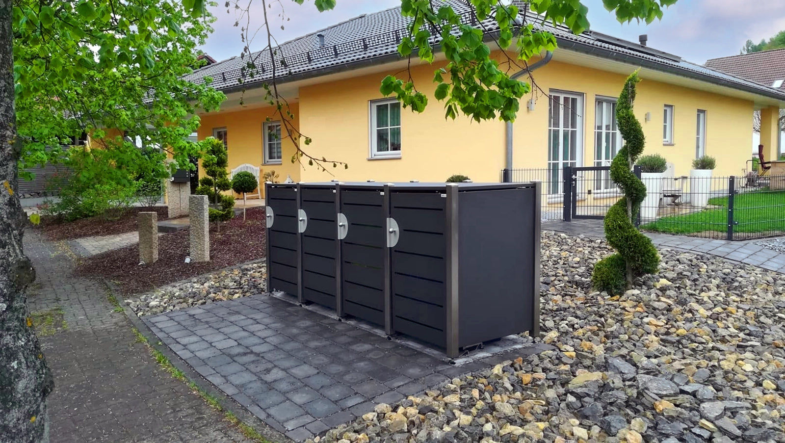 Vierfach-Anlage HALABOX Modular mit Türdesign in Lamellenoptik neben einem Wohnhaus